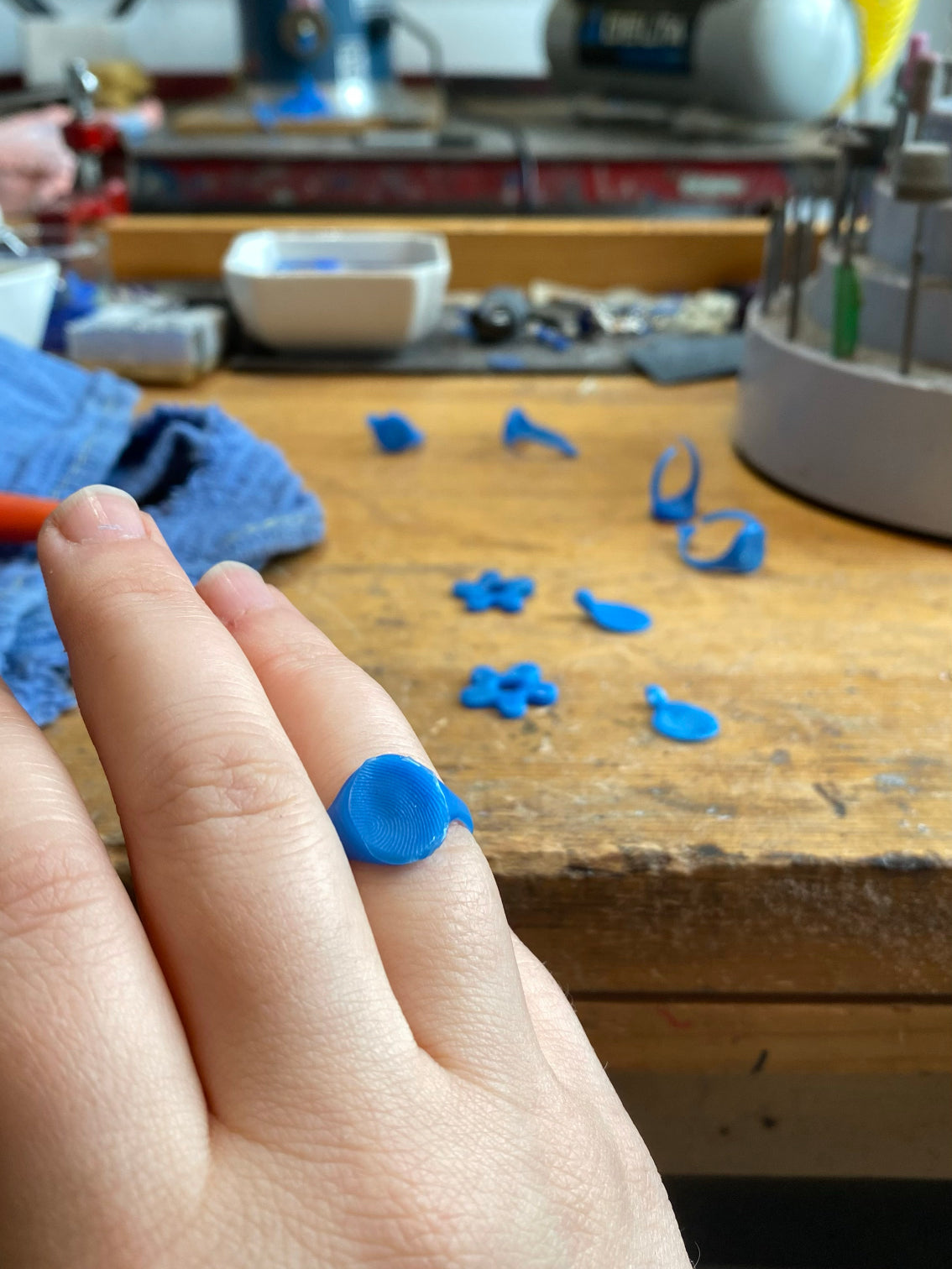 Lost wax models of fingerprint pieces on table with fingerprint signet ring on hand